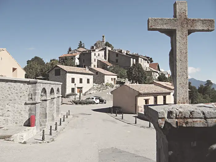 Place du village devant le lavoir et l'église Saint-Michel dominant le village, à Ilonse